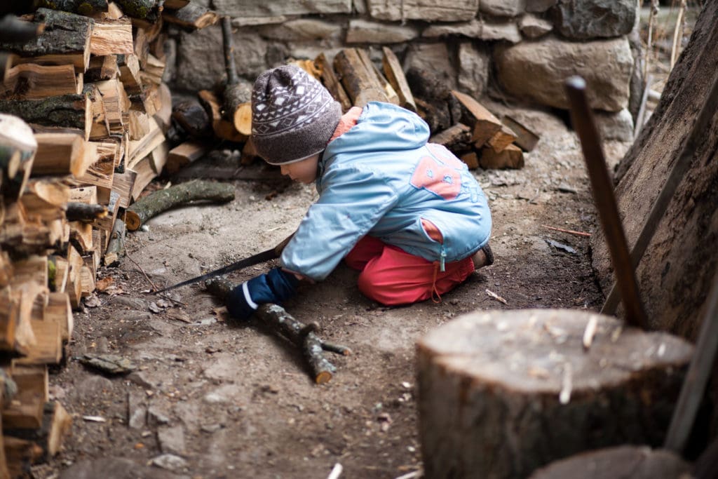 Boy cutting wood with a saw, sitting on his knees